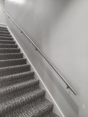 Round stainless wall handrail running up a carpeted commercial stair