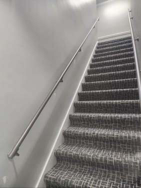 Round stainless wall handrail running up a carpeted commercial stair