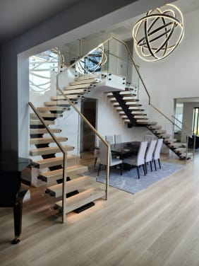FLIGHT Mono stairs with oak treads and glass railing on standoff pins lead to a glass-railed balcony over a dining area.