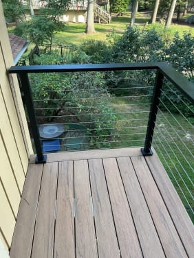 Black-post cable railing frames a small composite deck corner overlooking a garden.