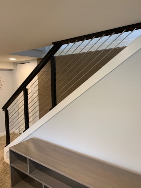Black cable railing runs above a white knee wall and along a stair opening beside built-in shelving.