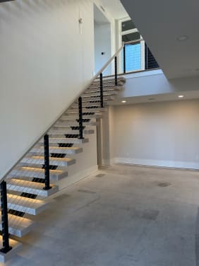 White oak floating treads with LED lighting on a mono stringer with black cable railing rising to a loft.