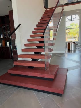Red-stained stacked plinth boxes at the base of a FLIGHT mono stair with frameless glass railing.