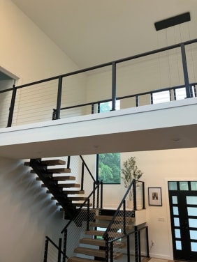 Light oak treads on a black mono stringer switchback with black cable railing continuing along the loft above.