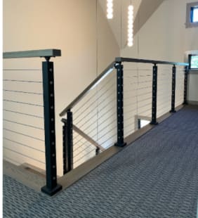 Black posts with stainless cable infill and a wood cap rail around a carpeted stair landing.