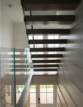 White oak cantilever treads float along a paneled wall beside frameless glass
