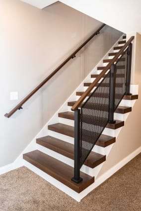 Dark stained thick-nose replacement treads with white risers pair with a black perforated panel railing and wall handrail.