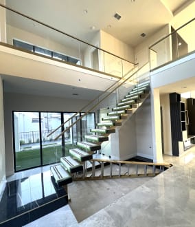 Floating stair with champagne-finish glass railings rising to a loft beside a glass wall onto a courtyard
