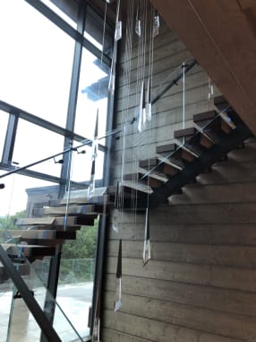 Floating stair with glass railing rising beside a wall of windows and weathered wood planks