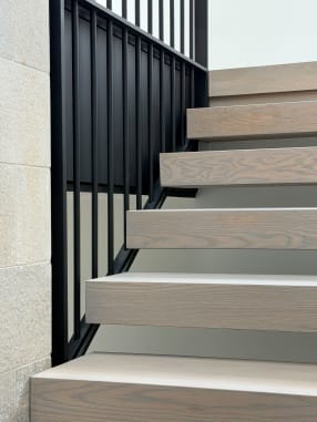 Gray oak stack treads beside a wall of black vertical balusters and stone cladding.