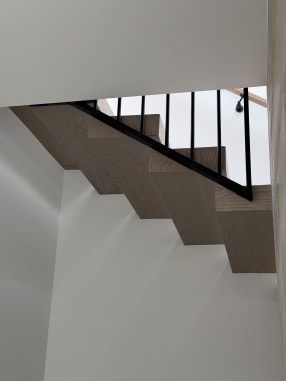 Zig-zag underside of a gray oak stack stair with black vertical balusters and wall handrail.