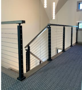 Black posts with stainless cable infill and a wood cap rail around a carpeted stair landing.