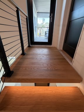 Wide white oak floating landing with onyx black rod railing toward a glass door