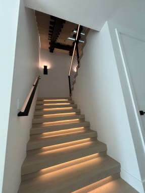 White oak stair treads with warm LED lighting and a black wall-mounted handrail