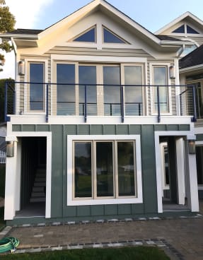 Black cable railing spans an upper balcony across a cream-and-green lake house facade.