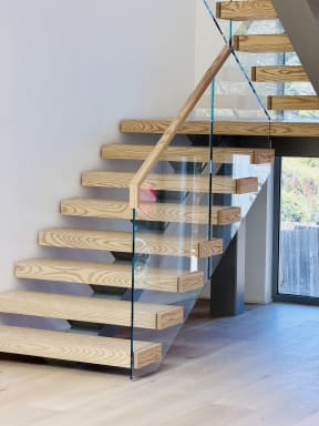 Close view of thick ash floating treads with frameless glass and a wood handrail