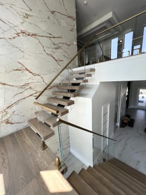 Floating oak stair with glass on brass talons and a gold handrail against a marble wall