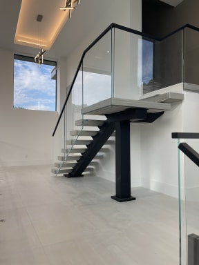 White floating switchback stair on a black steel stringer and column with frameless glass and black handrail