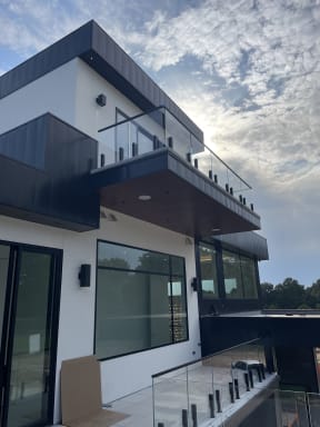 Frameless glass on black talon spigots lines the balcony of a modern black-and-white home