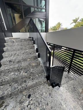 Solar gray glass on side-mount ascend talons with a black handrail down terrazzo exterior stairs