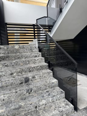 Terrazzo stairs with solar gray glass panels on side-mount talons and a black handrail