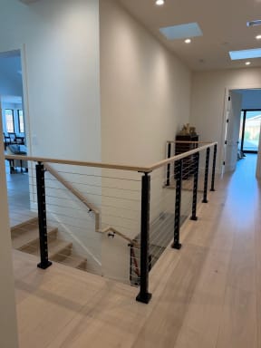 Black-post cable railing with a white oak cap wraps a stair opening in a bright hallway with skylights