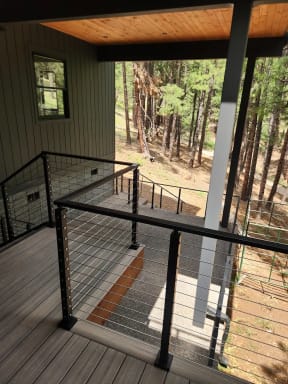 Black cable railing frames a covered balcony above a pine-forested hillside