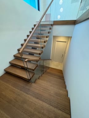 Walnut floating stair with frameless glass and wood handrail descending through a bright stairwell