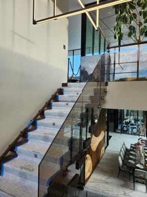 Floating stair with standoff-pin glass rising over an elegant dining room with a live-edge feature wall