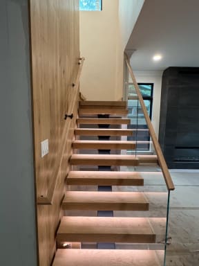White oak floating stair with LED treads, frameless glass and a wall-mounted oak handrail
