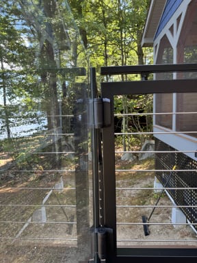 Jet black gate with rod infill meeting frameless glass on a lakeside deck