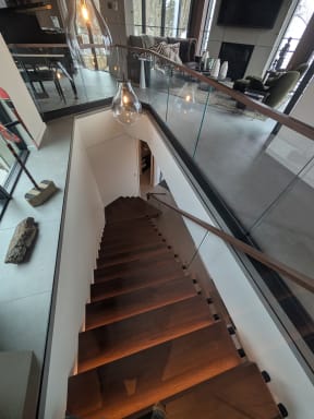 Walnut floating treads with LED lighting below a standoff-pin glass railing and walnut cap
