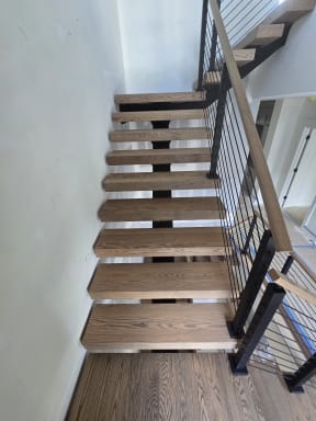 Red oak floating treads on a black mono stringer with black rod railing and oak handrail turning at a landing