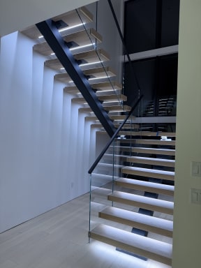 White oak FLIGHT Mono switchback with glowing LED treads and frameless glass in a tall white stairwell