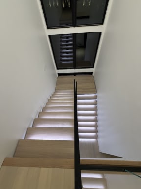 Looking down LED-lit oak floating treads with a slim glass railing