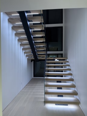 Pale oak floating switchback stair with cool LED tread lighting and frameless glass