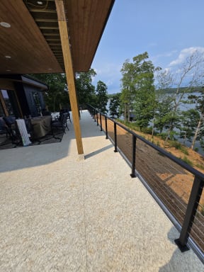 Black cable railing runs along a long covered terrace above a wooded lake shore