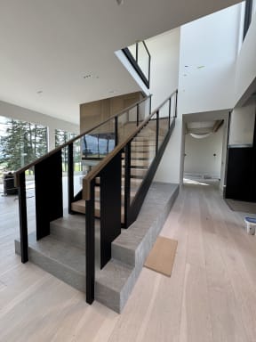 Twin black steel plate stringers and glass railing with walnut handrail on a stone-plinth stair
