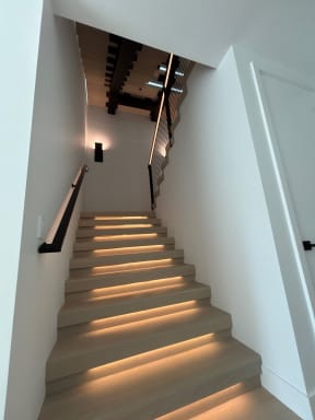 White oak stair treads with warm LED lighting and a black wall-mounted handrail