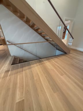 Frameless glass with an oak handrail guards a stair opening on wide white oak floors