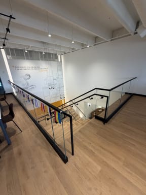 Frameless glass with black handrail wraps an office stair opening on wood floors