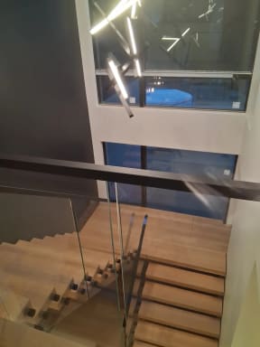 White oak floating switchback treads beside frameless standoff-pin glass and a black handrail
