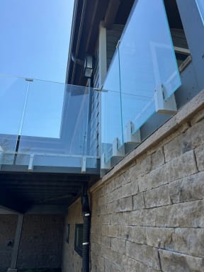 Frameless glass on silver side-mount brackets above a stacked-stone wall