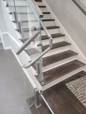 Stainless post glass railing with a looped stainless handrail return at a stair base