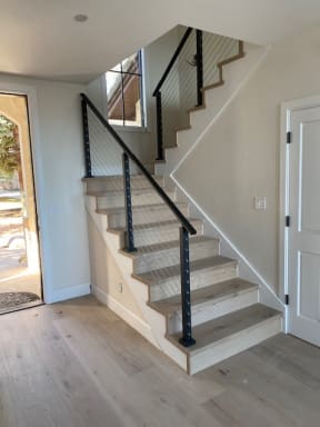 Black-post cable railing and handrail climb a white oak stair beside an arched door