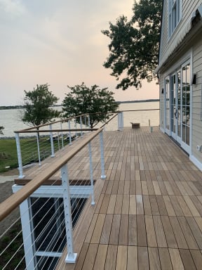 A hardwood deck wraps a lake house, edged with white-post cable railing and a wood handrail at dusk.