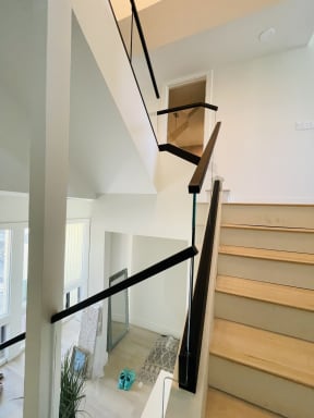 Glass railing with a slim black handrail in a black channel climbs a white oak switchback stair.