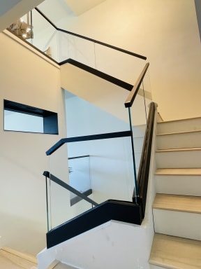 Frameless glass with a square black handrail follows a white oak stair through multiple landings.