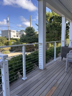 White aluminum posts and stainless cables line a covered hardwood porch with garden views.