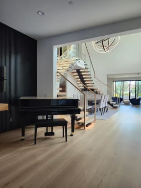 A grand piano sits in the foreground with FLIGHT Mono stairs and standoff-pin glass railing in the room beyond.